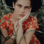 Artistic close-up portrait of a woman in a floral dress and hat outdoors.
