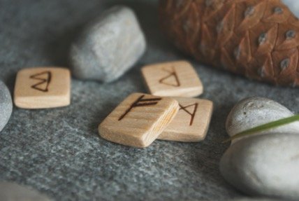 Pièces de runes en bois posées sur des pierres dans une ambiance naturelle.