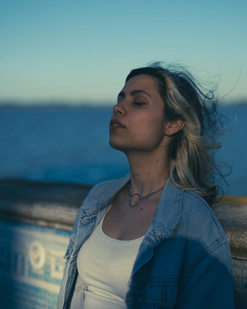 Femme en veste en jean, moment de sérénité au bord de l'eau, illustrant le retour au calme après un épuisement