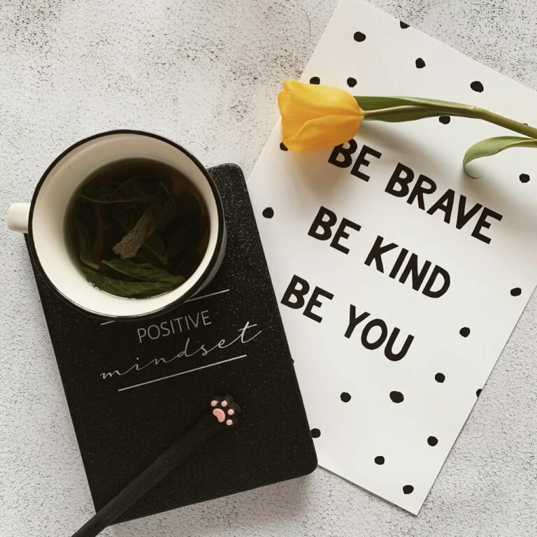 Tasse de tisane posée sur un carnet “positive mindset”, avec une fleur jaune et une carte inspirante, pour illustrer le concept de bien-être pansement