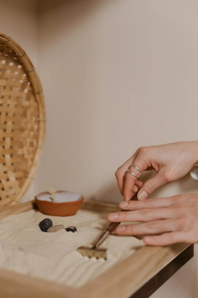 Mains qui tracent des lignes dans un jardin zen miniature, sable et pierres, geste répétitif apaisant contre le stress chronique
