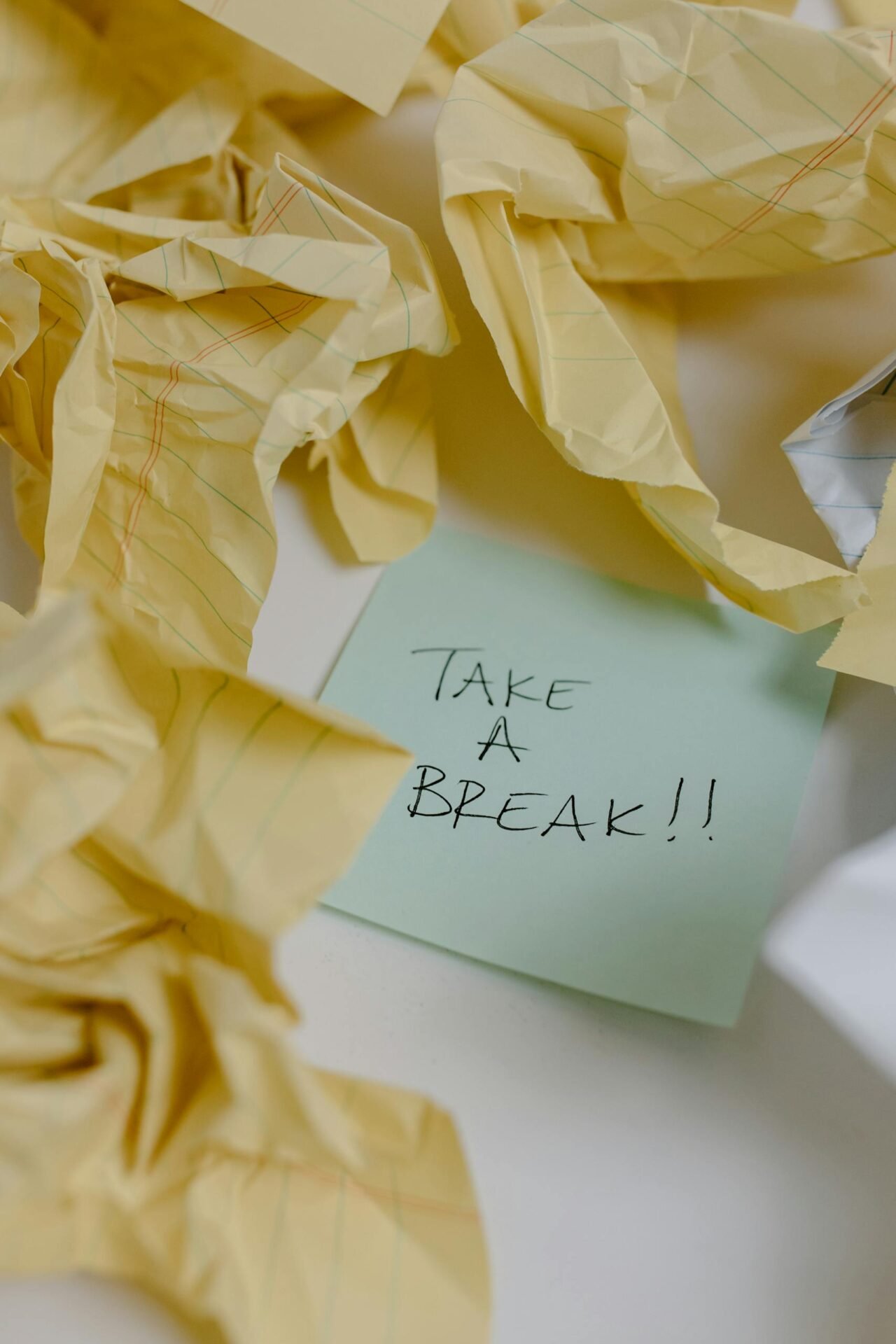 Post-it avec l'inscription "Take a break" entouré de papiers froissés, symbole de surcharge mentale et d'épuisement au travail